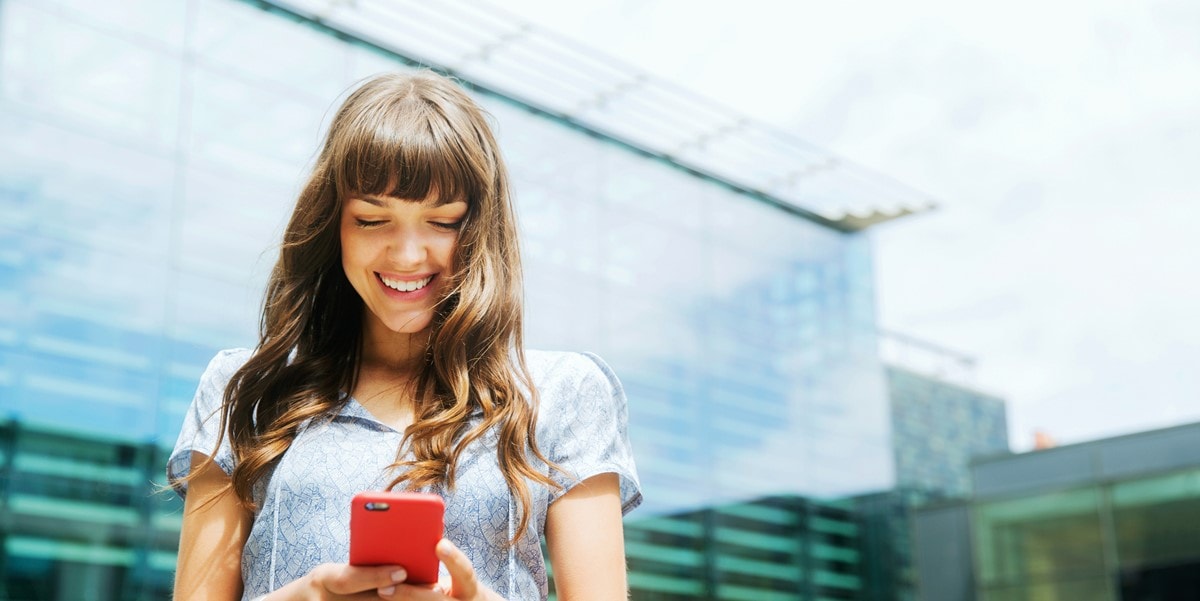 young woman standing in front of building, looking down at phone