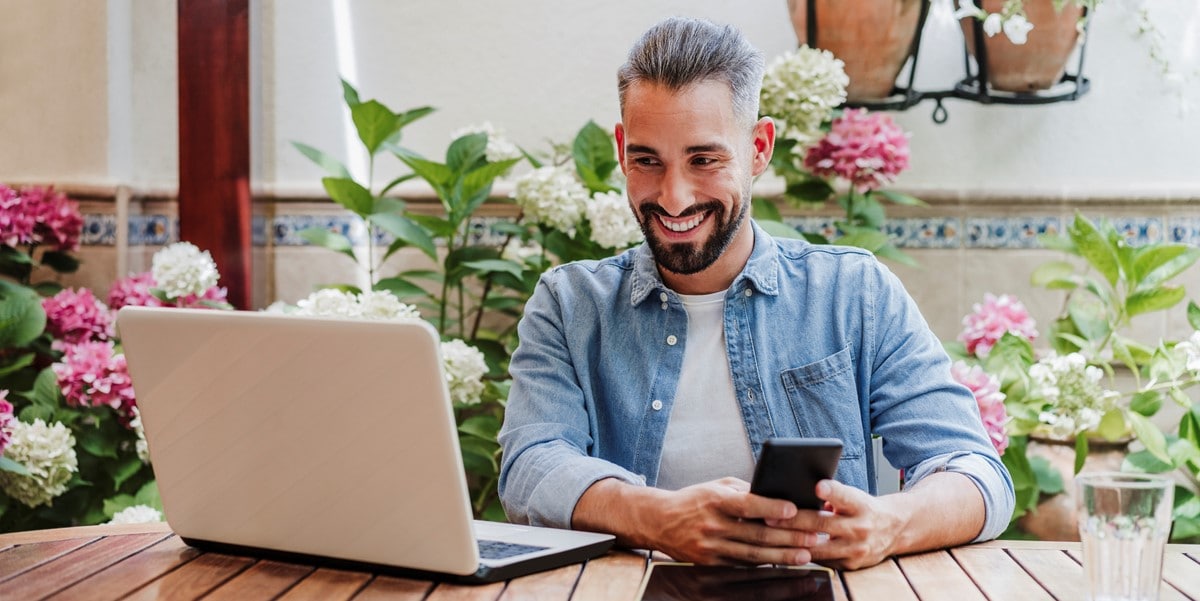 man working at a table, using laptop and cell phone