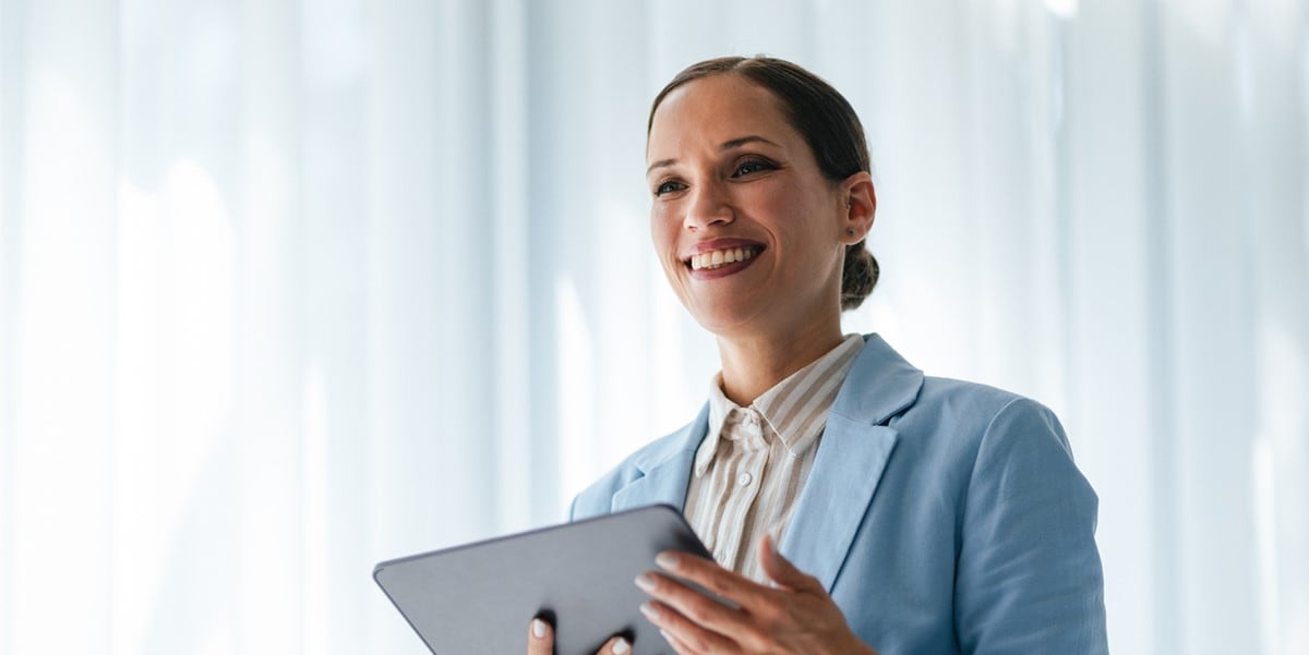 woman in blue suit jacket, smiling with tablet in hands